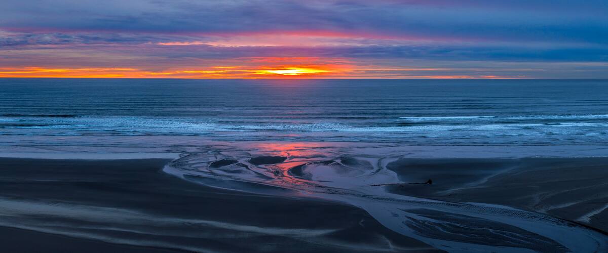 A sunset over a beach with calm waves and a clear sky.