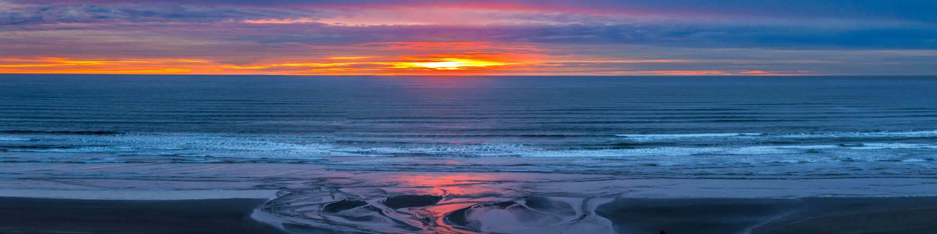 A sunset over a beach with calm waves and a clear sky.