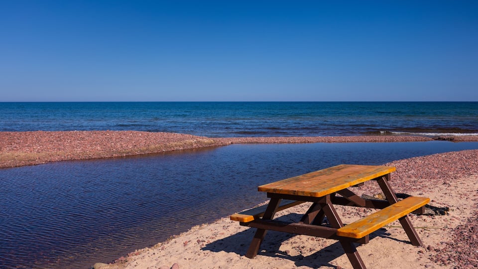A wooden picnic table on a sandy beach with a calm sea in the background.