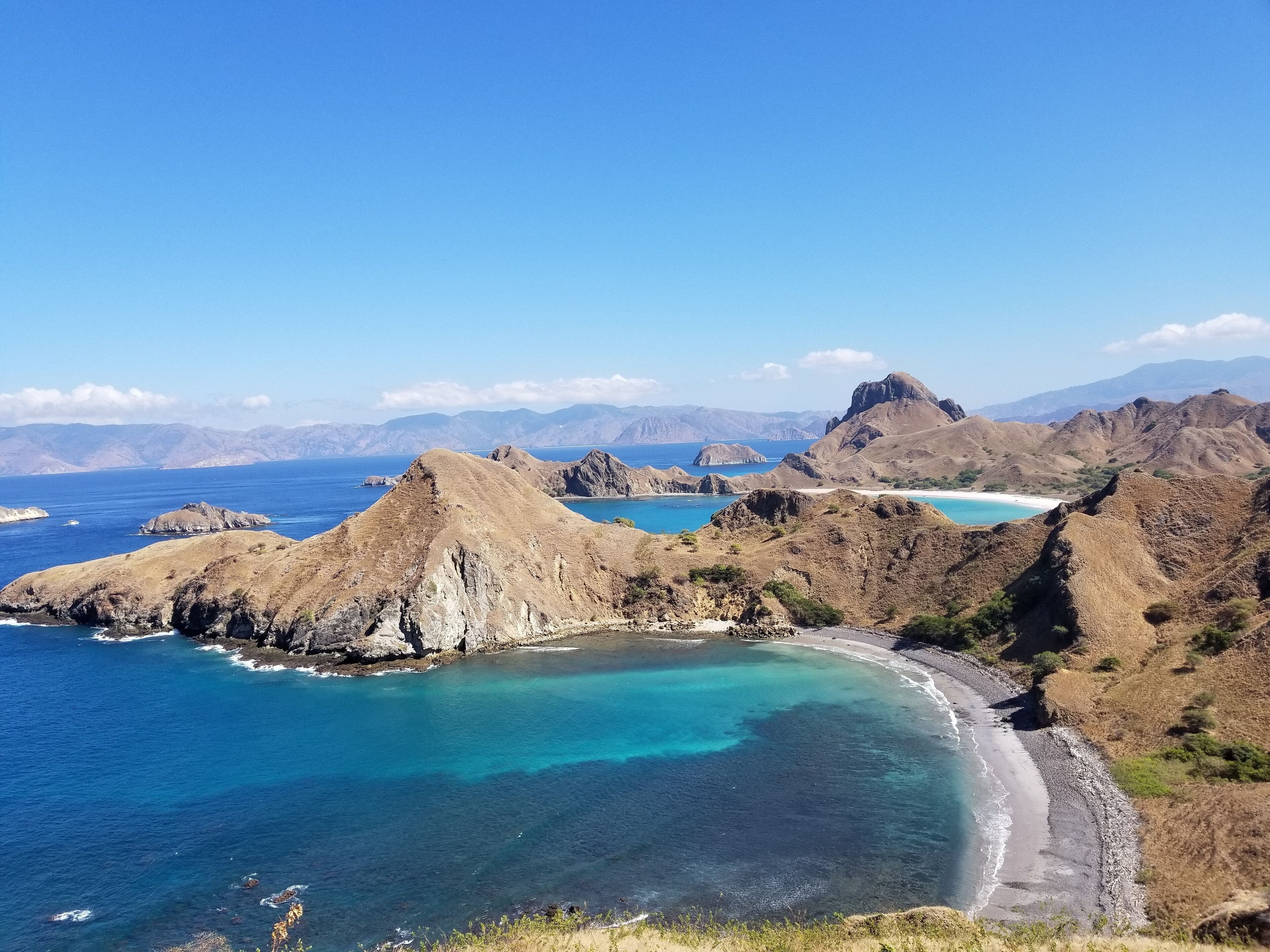 A coastal landscape with rugged mountains, clear blue waters, and a sandy beach.