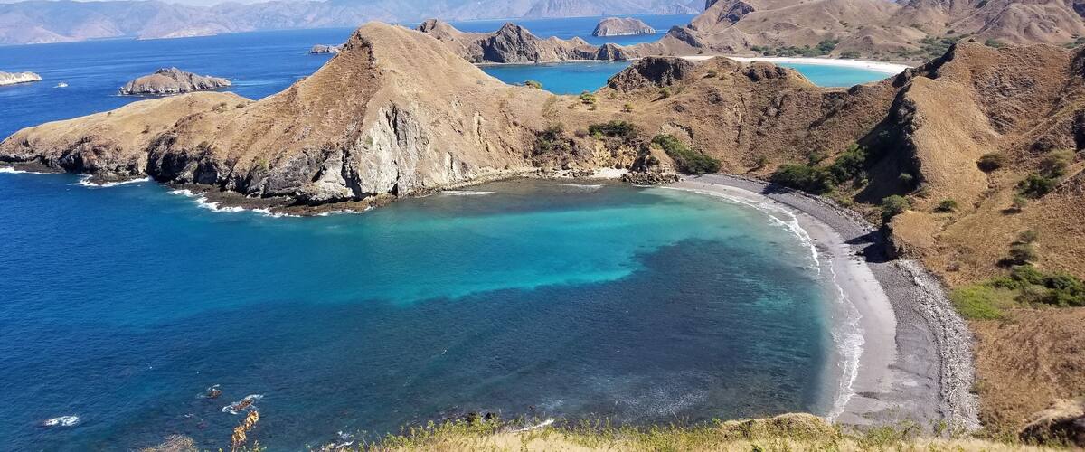 A coastal landscape with rugged mountains, clear blue waters, and a sandy beach.