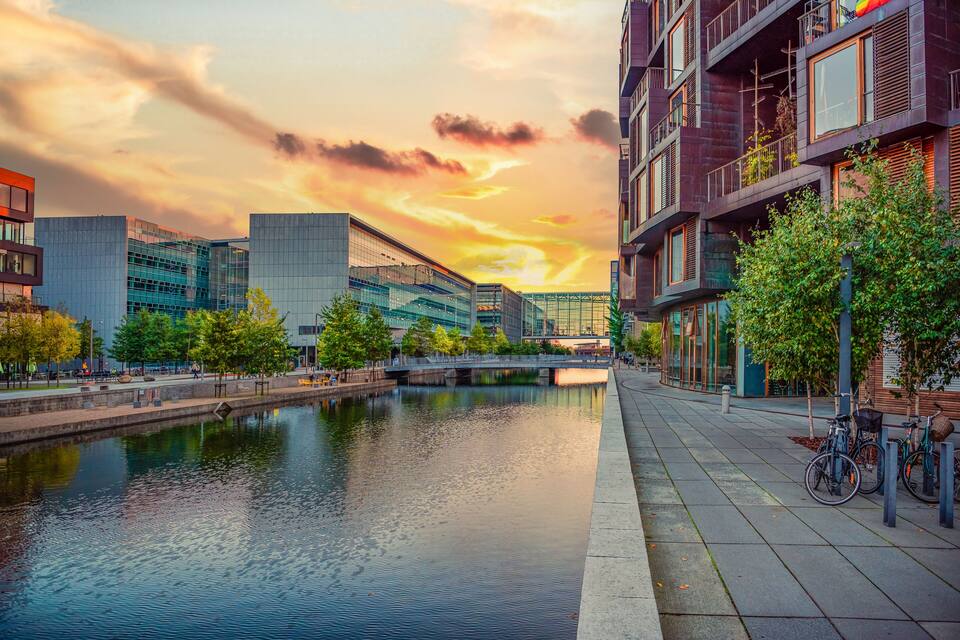 A river with modern buildings and a sunset sky.