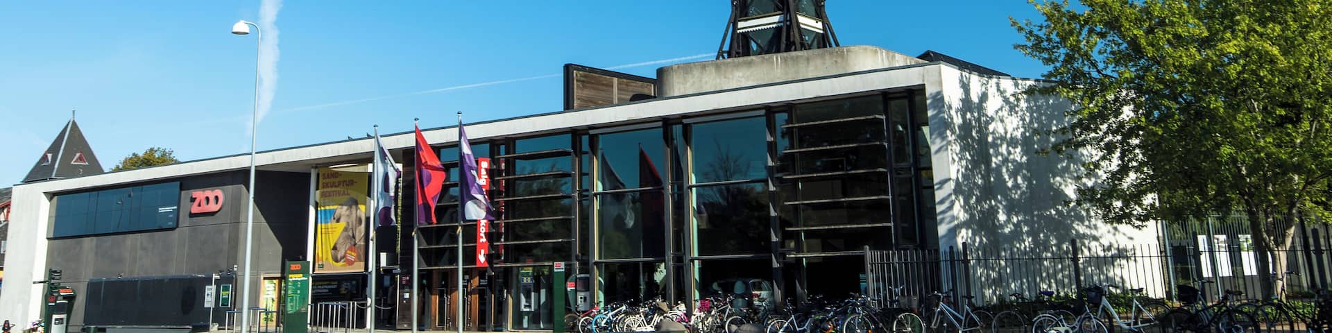 A modern building with a tower, a flag, and bicycles parked in front.