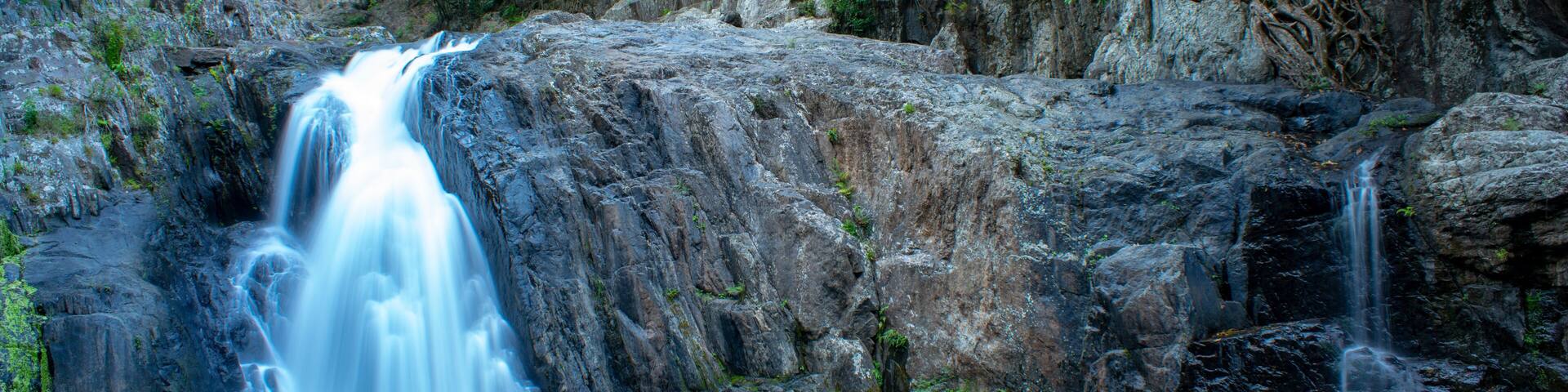 A waterfall cascading over a rocky cliff surrounded by dense green foliage.