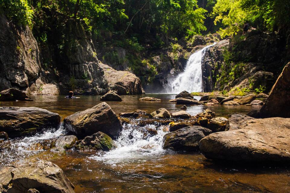 Una cascada en un área boscosa con rocas grandes al frente.