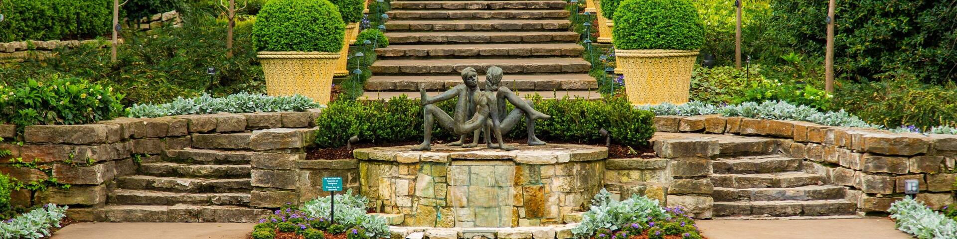 A garden with a statue of two figures, stone steps, and well-manicured hedges.