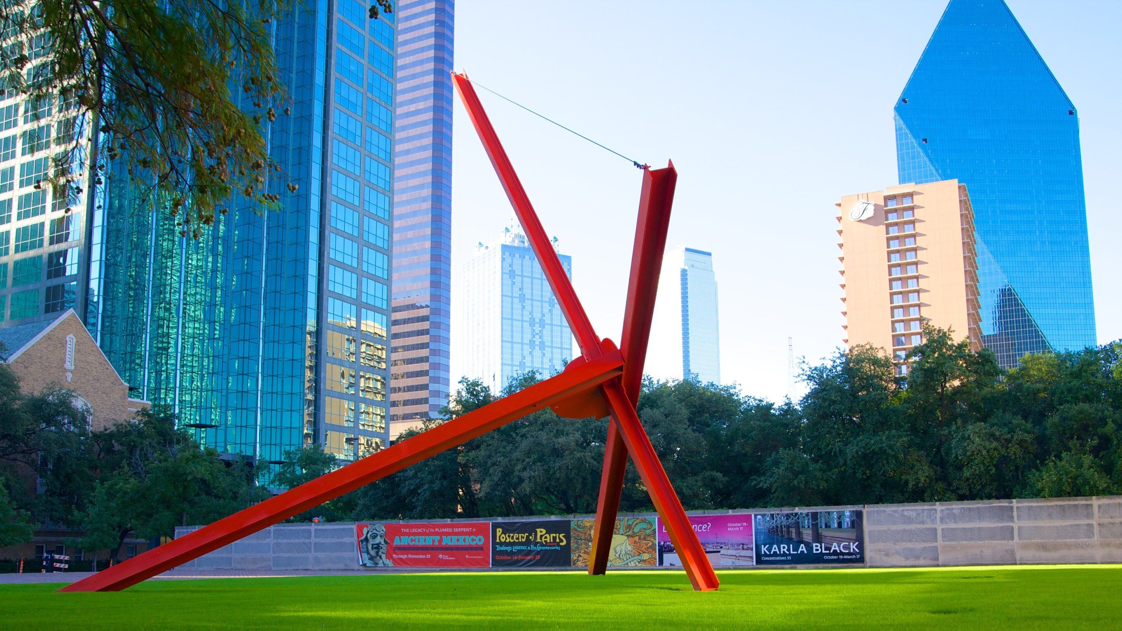 A modern sculpture in a park with tall buildings in the background.