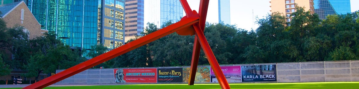 A modern sculpture in a park with tall buildings in the background.