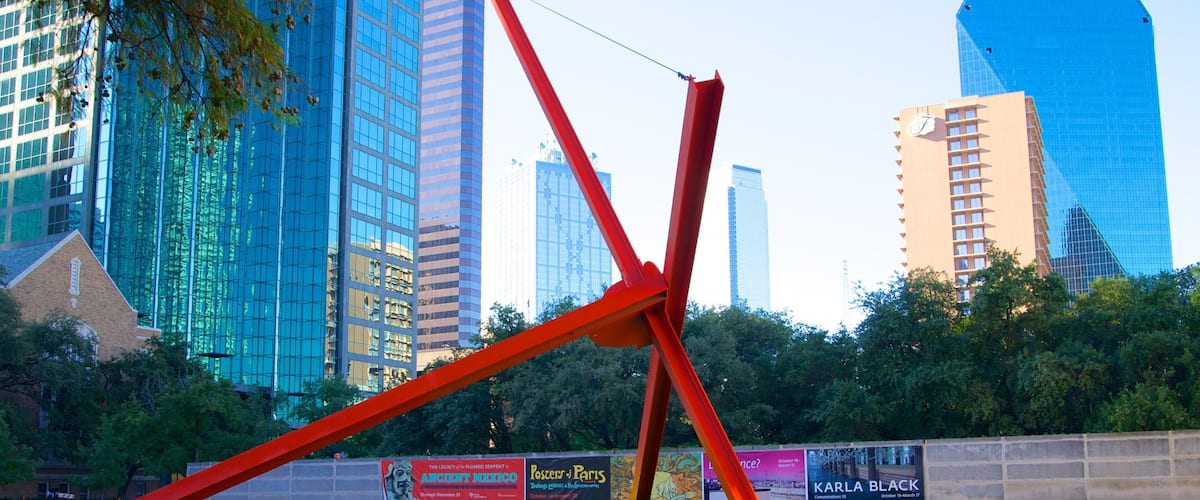 Eine moderne Skulptur in einem Park, im Hintergrund hohe Gebäude.