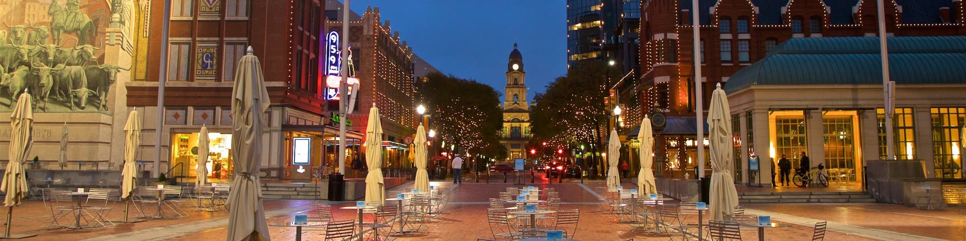 A city square with outdoor seating, a historic building with a mural, and a modern skyscraper in the background.