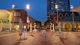 Una plaza urbana con mesas al aire libre, un edificio histórico con un mural, y un rascacielos moderno al fondo.
