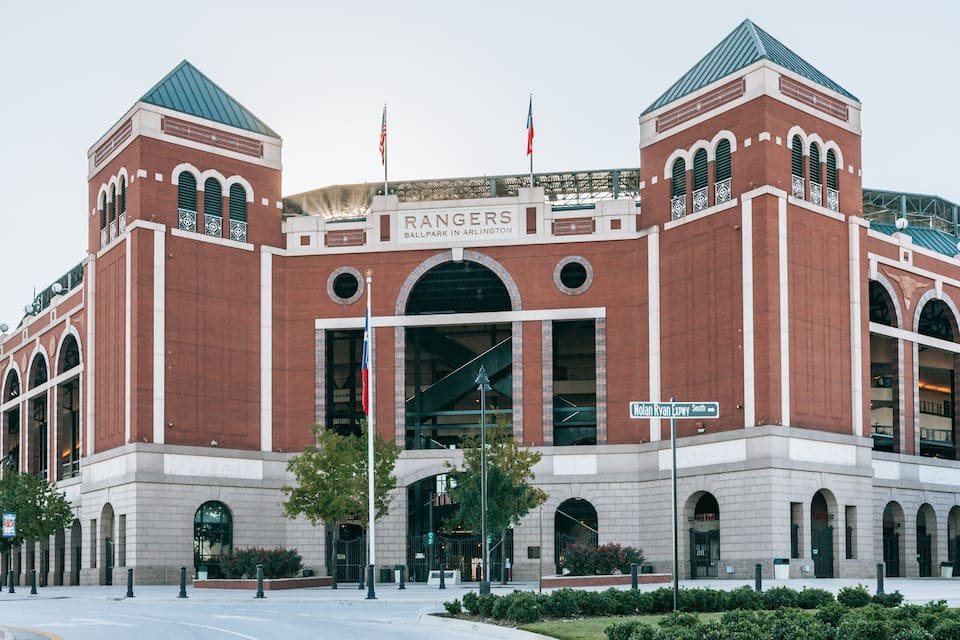 Un grande stadio in mattoni con finestre ad arco e due torri, chiamato 'Rangers Ballpark in Arlington'.