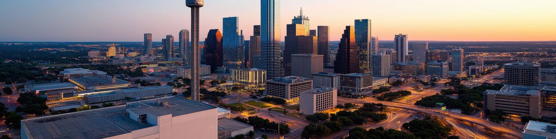A city skyline at dusk with a tall building in the middle. The city is lit up with lights and the sky is a beautiful orange color