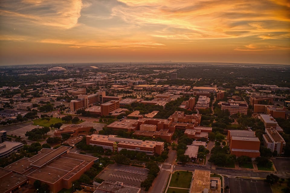 Une vue aérienne d’une ville au coucher du soleil, avec un bâtiment remarquable en forme de dôme et un mélange de bâtiments commerciaux et résidentiels.