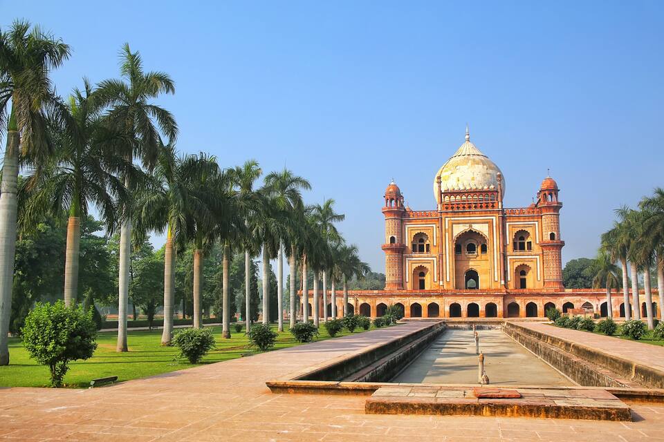 A large, ornate building with a dome and minarets, surrounded by palm trees and a well-maintained garden.