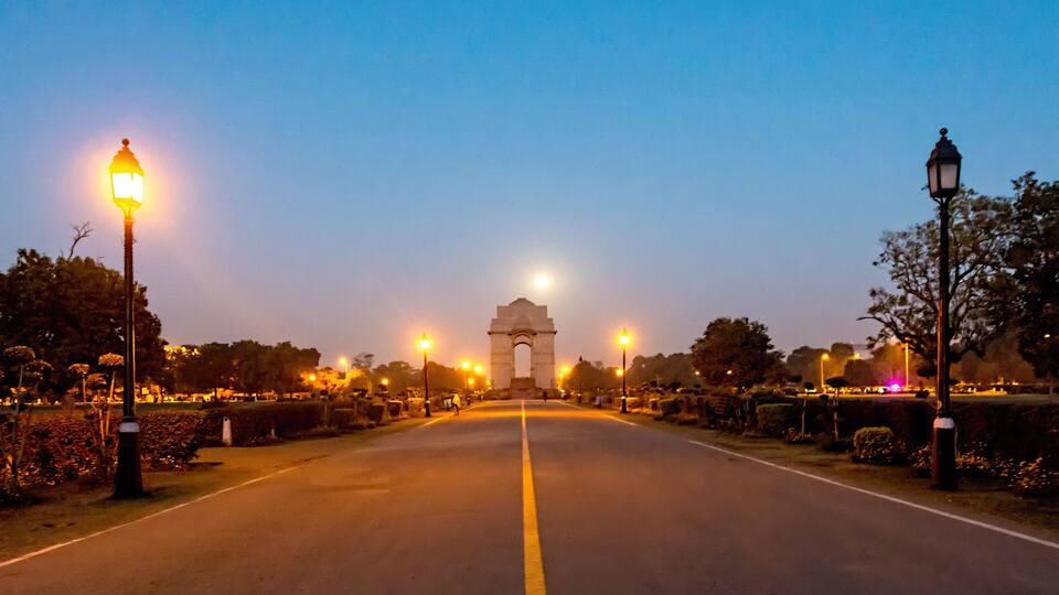 A road leading to a large arch monument, surrounded by trees and street lamps.