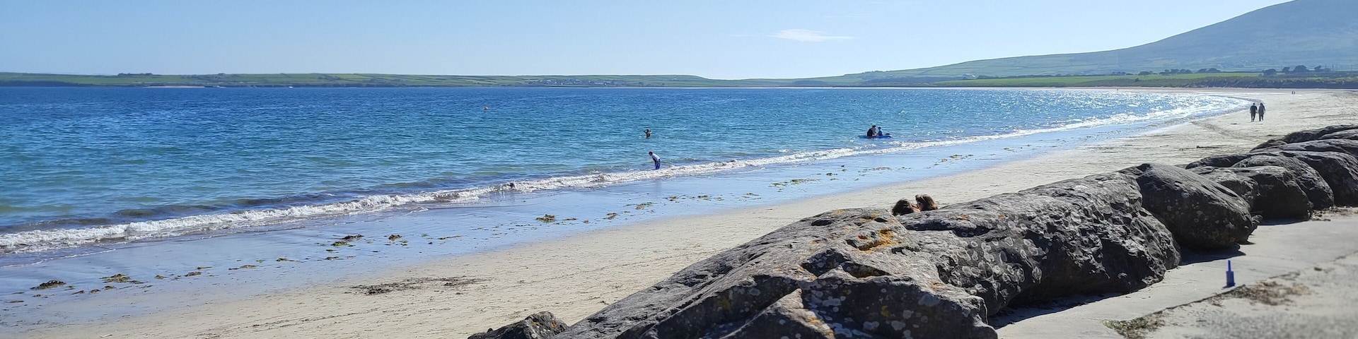 Una playa con costa rocosa, agua tranquila y colinas al fondo.