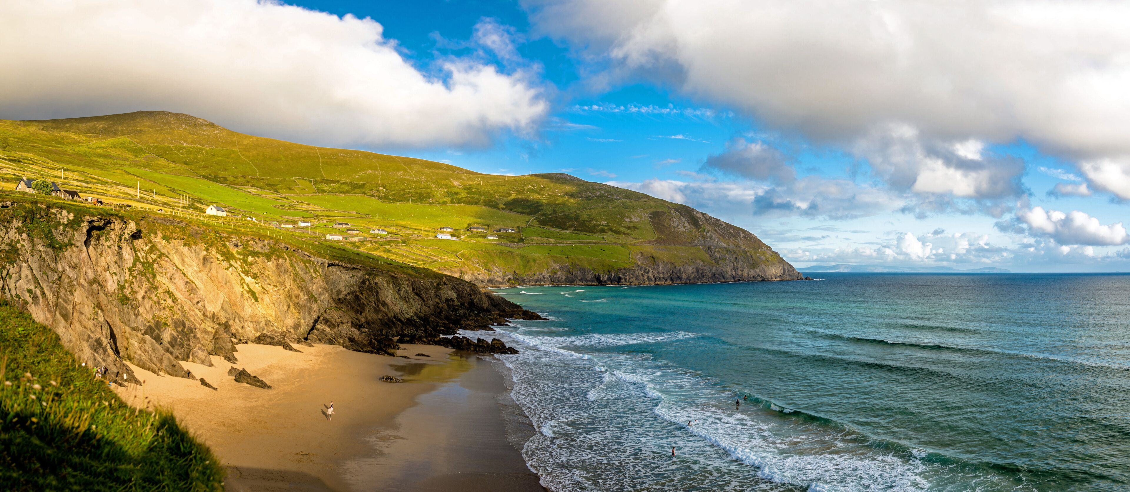 A coastal landscape with a sandy beach, green hills, and a clear blue sky.