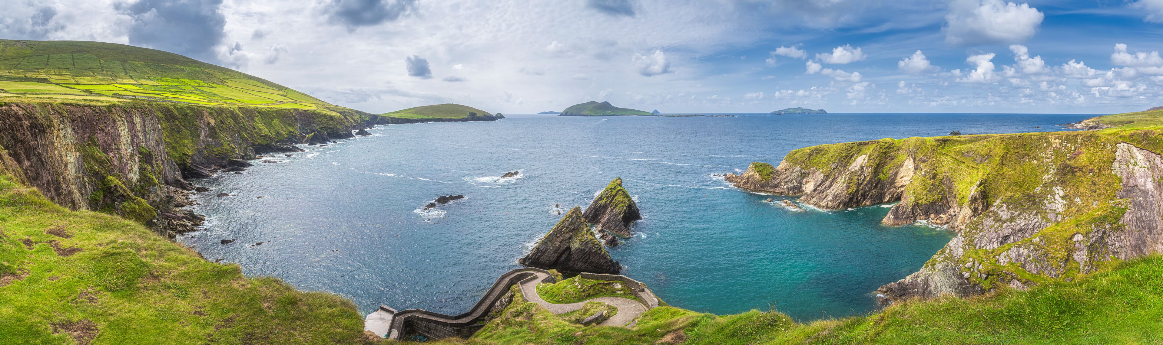 A coastal landscape with green hills, a winding path, and the ocean.