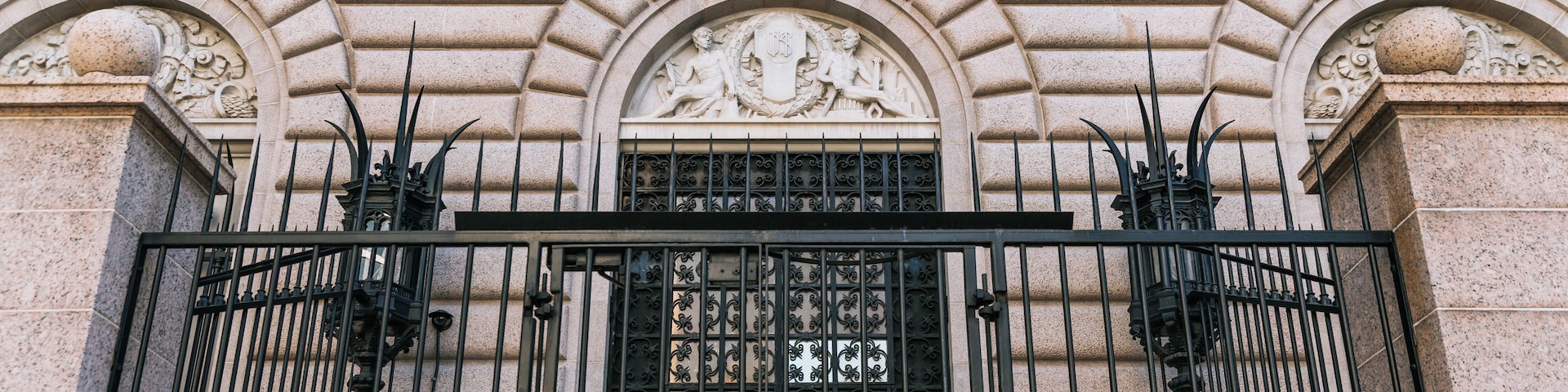 Eingang des Gebäudes der United States Mint mit aufwendiger Steinmetarbeit und Metallgittern.