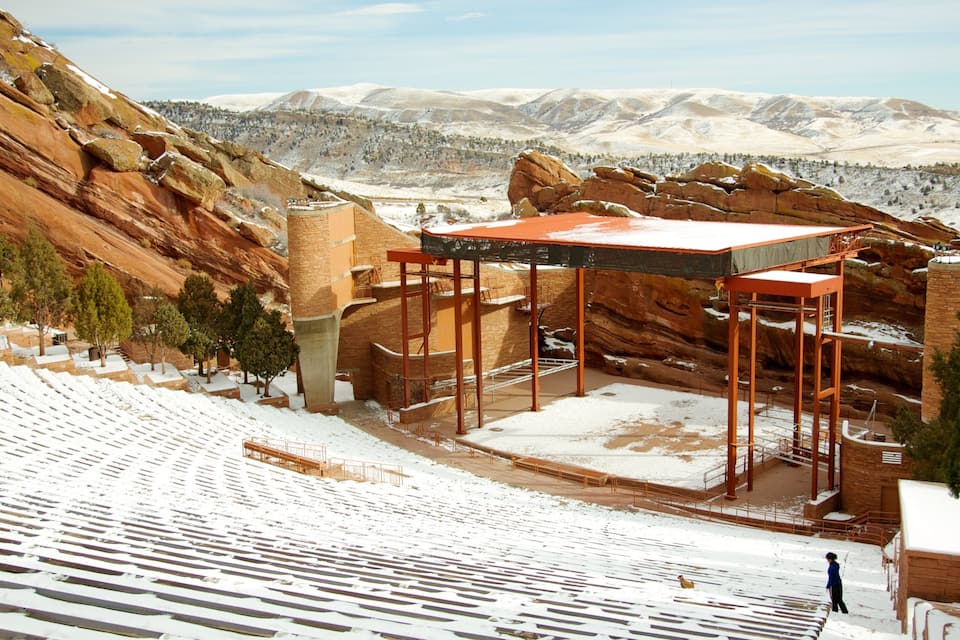 A snow-covered amphitheater with a red roof, set against a backdrop of red rock formations and distant mountains.
