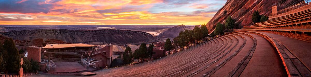 An outdoor amphitheater with tiered seating, a stage, and a large rock formation to the right.