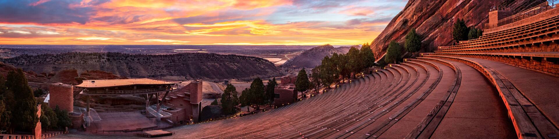 An outdoor amphitheater with tiered seating, a stage, and a large rock formation to the right.