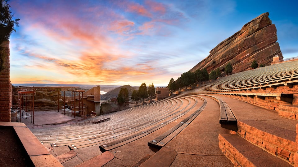 An outdoor amphitheater with tiered seating and a large rock formation in the background.