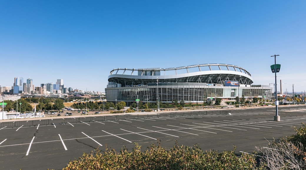 A large stadium with a modern design, surrounded by a parking lot and a city skyline in the background.