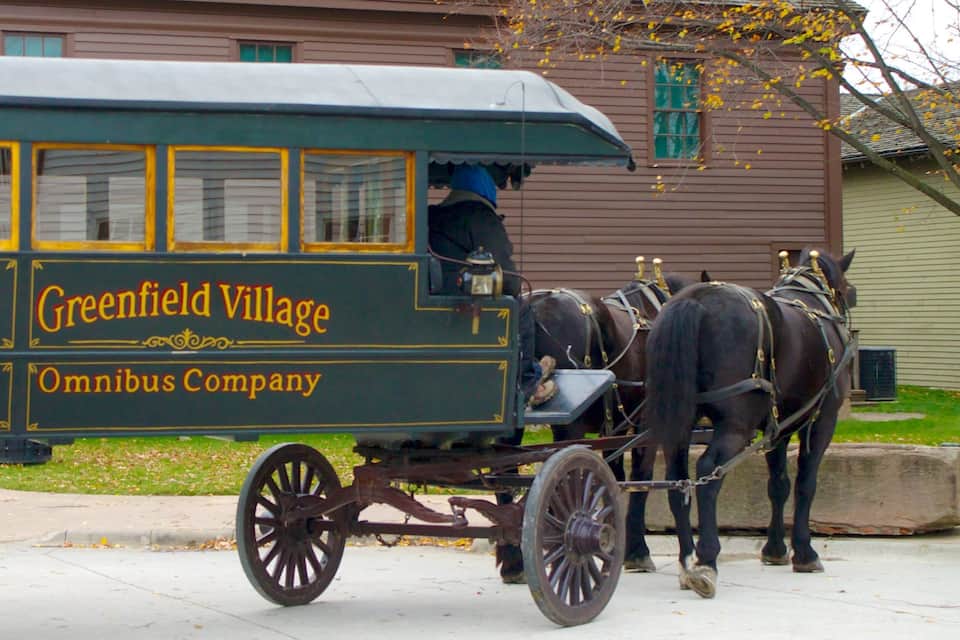 A horse-drawn carriage with the text "Greenfield Village Omnibus Company" on its side.