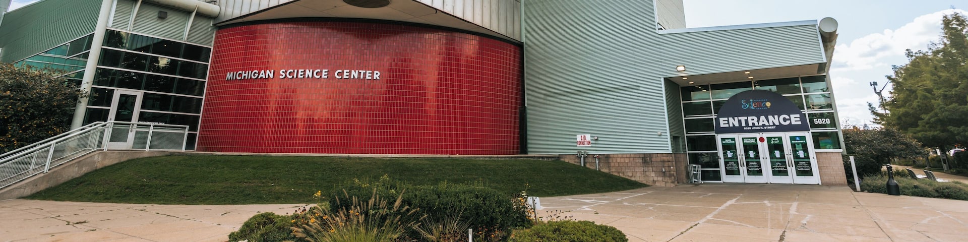 The Michigan Science Center building with a prominent red facade and a blue sign on the upper right.