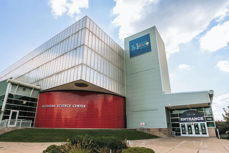 The Michigan Science Center building with a prominent red facade and a blue sign on the upper right.