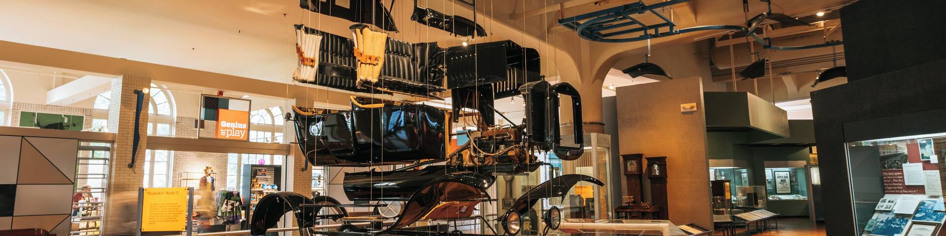 A museum exhibit with a large, suspended car and various mechanical parts.