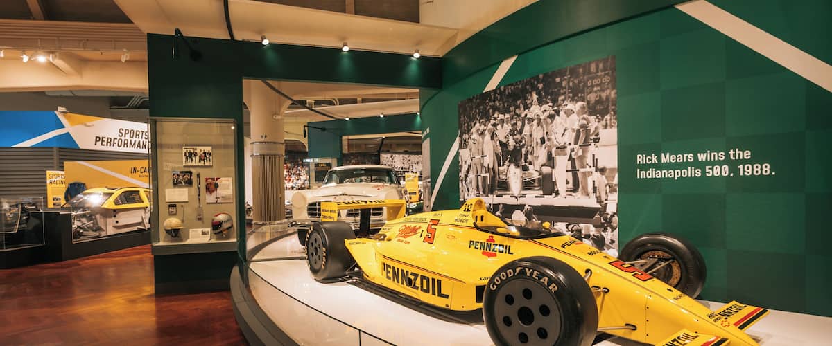 Un auto de carreras amarillo exhibido, con un texto que describe cómo Rick Mears ganó las 500 Millas de Indianápolis en 1988.