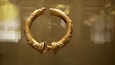 A golden circular artifact with intricate designs and a central knob, displayed against a blurred background.