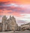 A historic church with Gothic architecture, a prominent clock tower, and a bridge in the background.