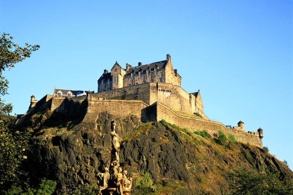 A historic castle on a hill with a statue in the foreground.