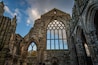 The ruins of Holyrood Abbey still stand tall silhouetted by blue sky and fluffy clouds behind the Queen's Gallery Palace in Edinburgh Scotland, UK