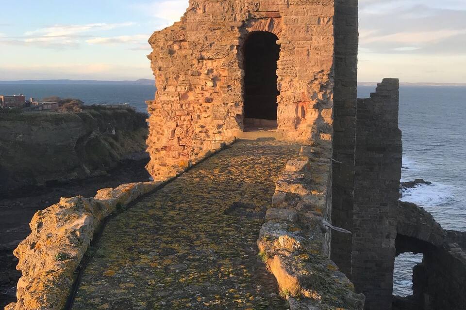 Un sendero de piedra que lleva a un arco deteriorado junto al mar.
