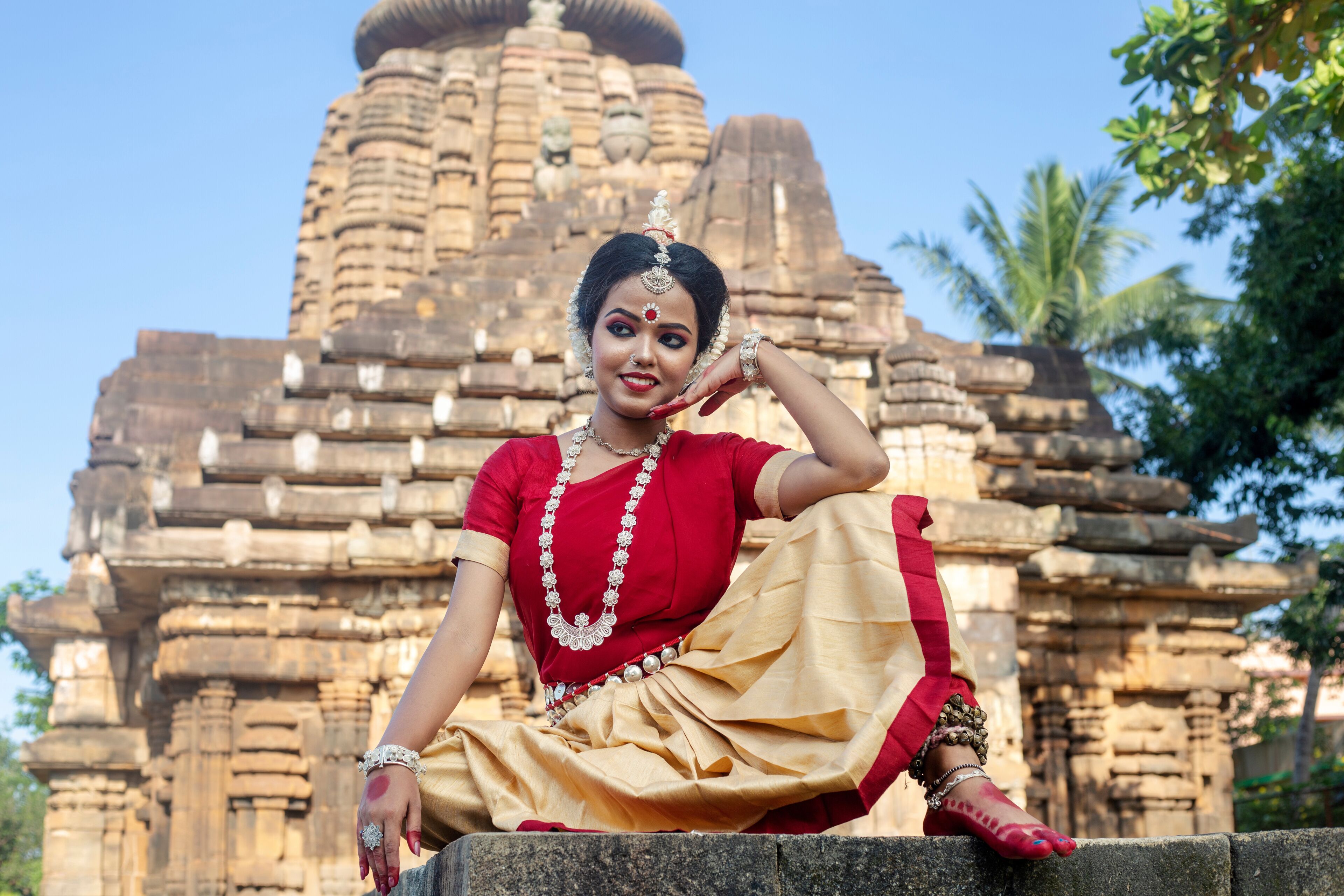 A person in traditional attire sitting in front of a stone temple with intricate carvings.