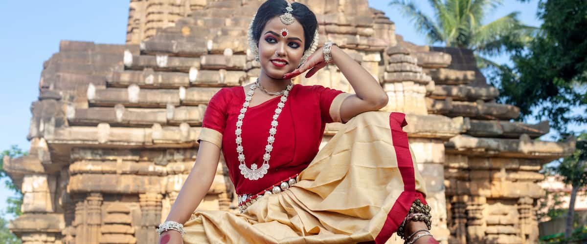 A person in traditional attire sitting in front of a stone temple with intricate carvings.