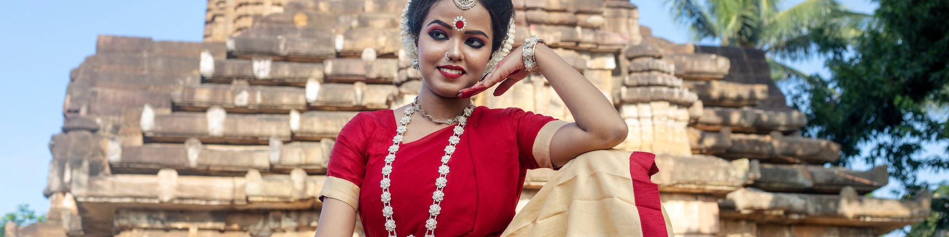 A person in traditional attire sitting in front of a stone temple with intricate carvings.
