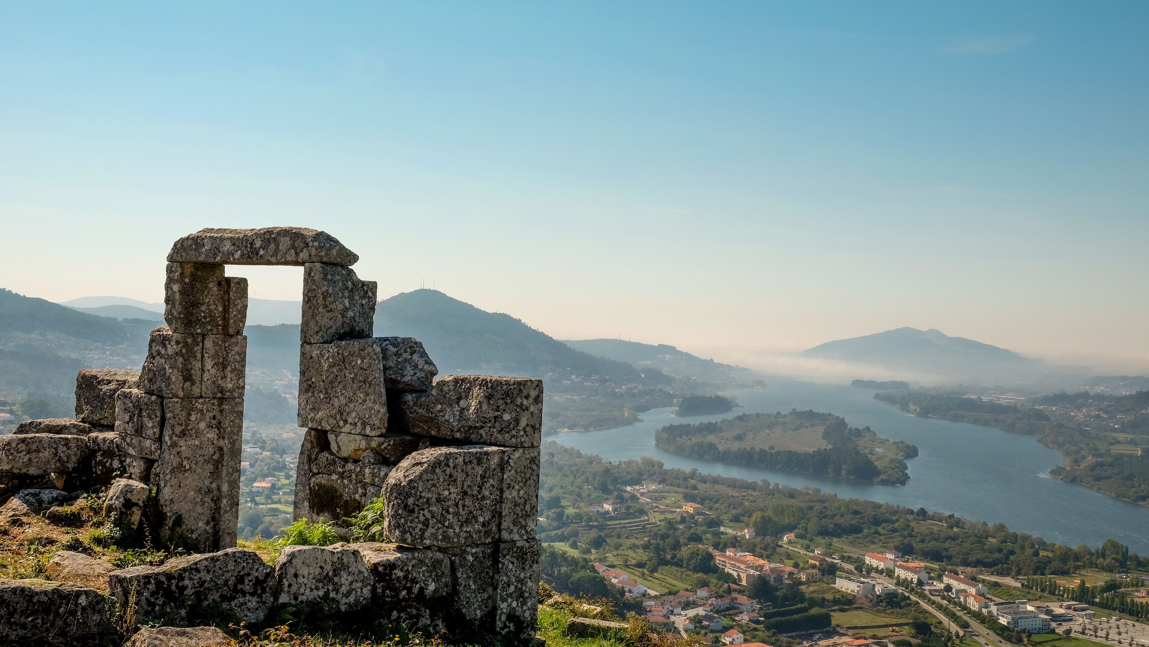 Ancient stone ruins, a river, and a town in the background.