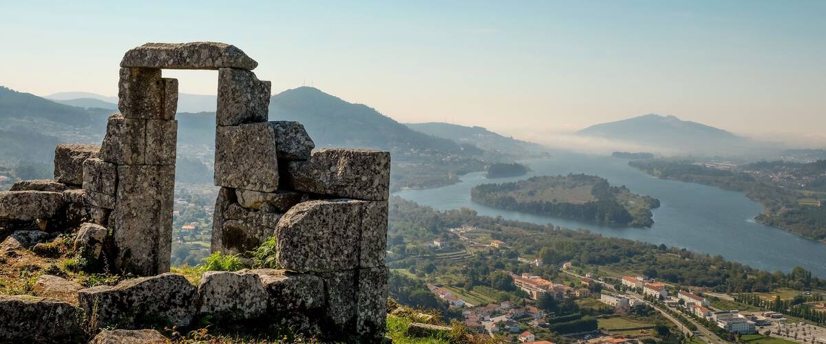 Ancient stone ruins, a river, and a town in the background.