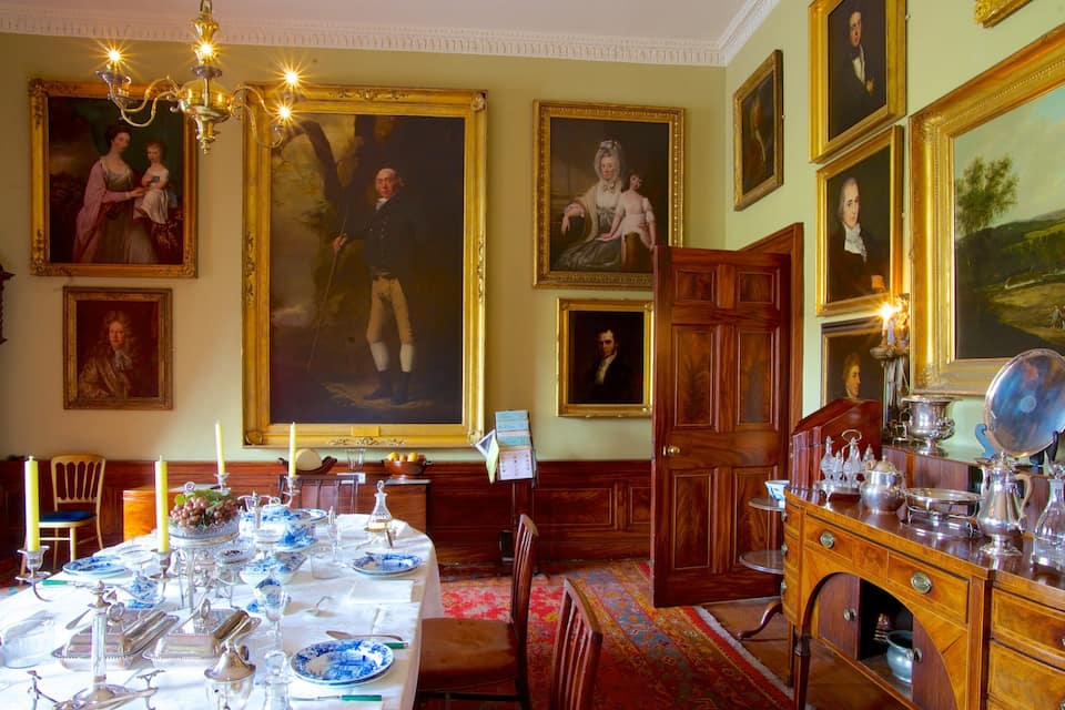 Une salle à manger élégante, avec une grande table dressée pour un repas, entourée de tableaux décoratifs et de meubles classiques.
