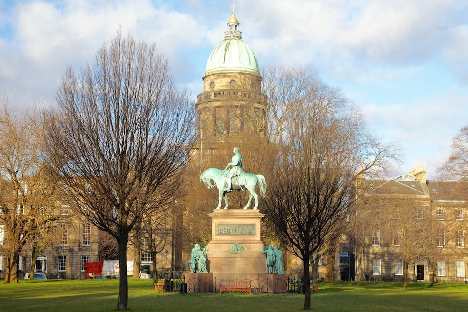 A statue of a man on horseback in a park with trees and a building in the background.