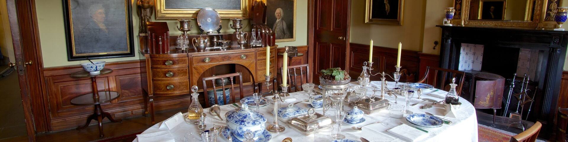 A formal dining room with a table set for a meal, surrounded by wooden furniture and framed portraits on the walls.