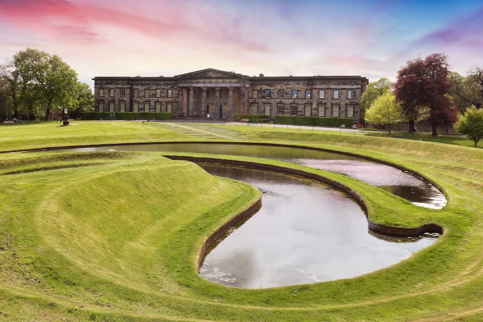 A large building with a formal facade, a well-manicured lawn, and a series of water features.