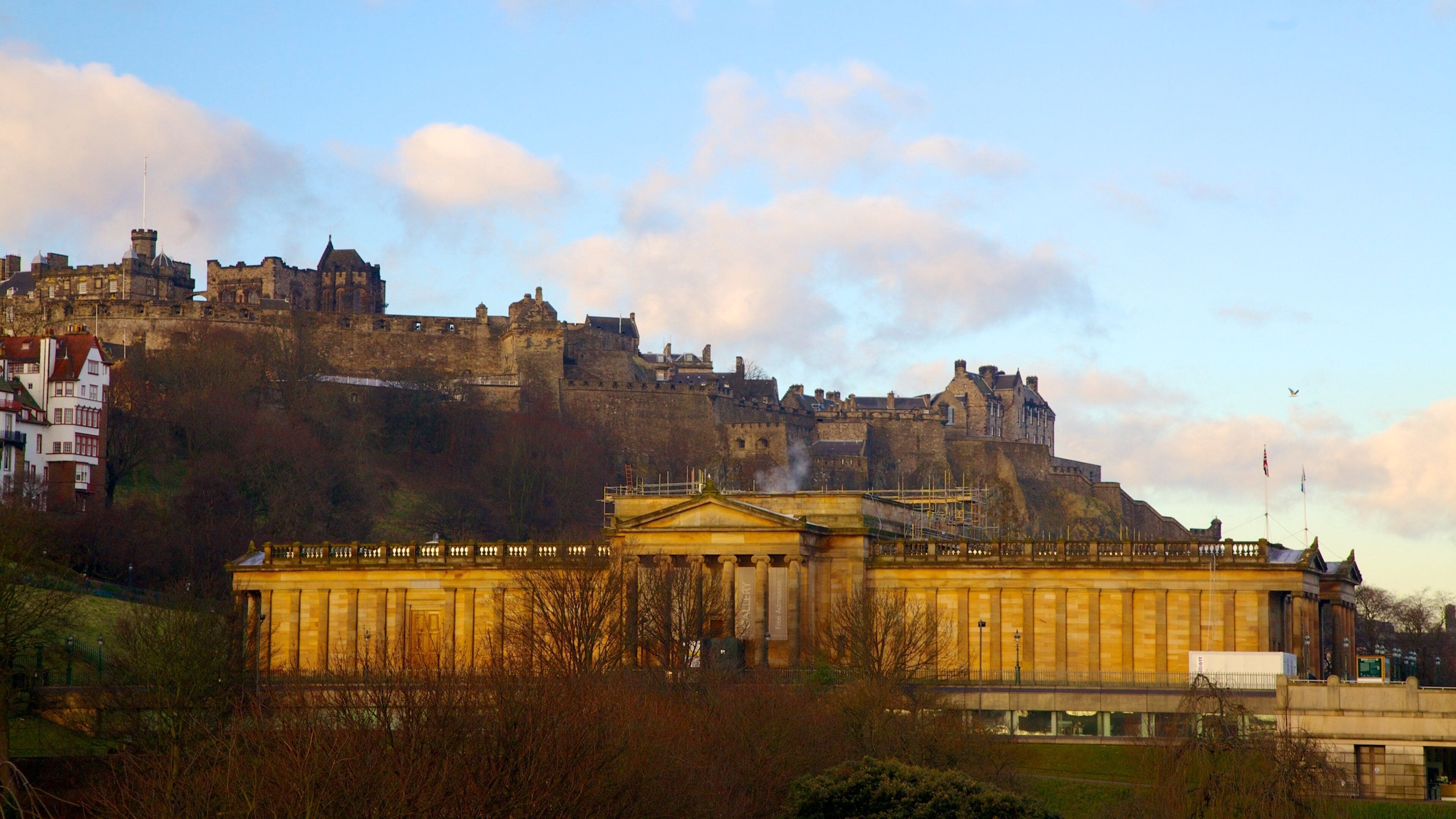 A historic castle on a hill with a classical building in the foreground.
