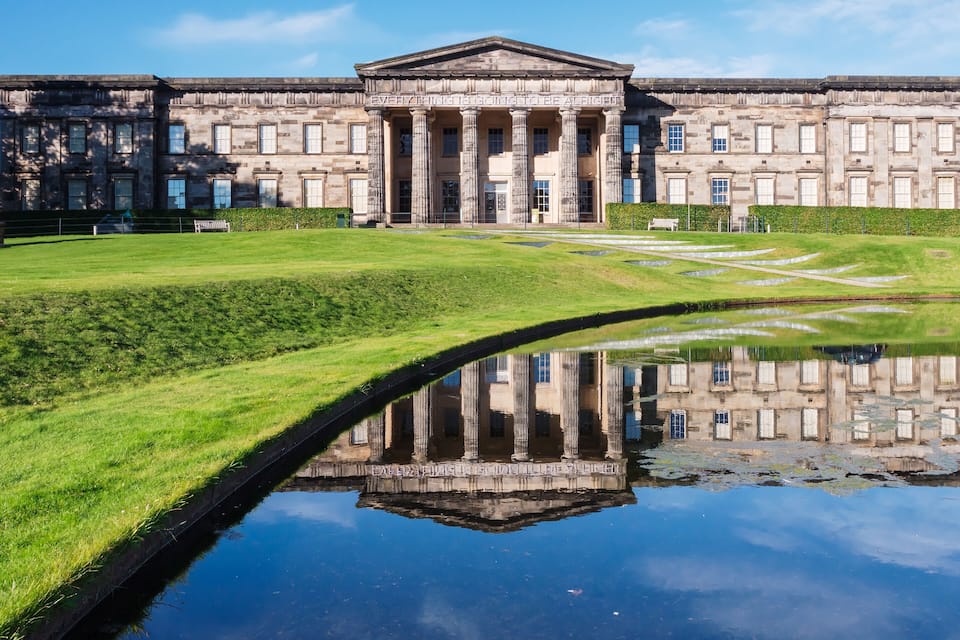 A classical building with columns and a reflective pond in front.